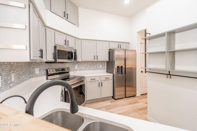 kitchen with decorative backsplash, stainless steel appliances, sink, a high ceiling, and light hardwood / wood-style floors