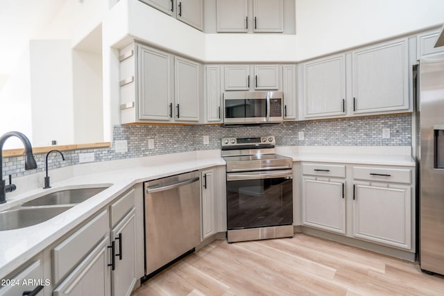 kitchen featuring sink, light hardwood / wood-style flooring, gray cabinets, appliances with stainless steel finishes, and tasteful backsplash