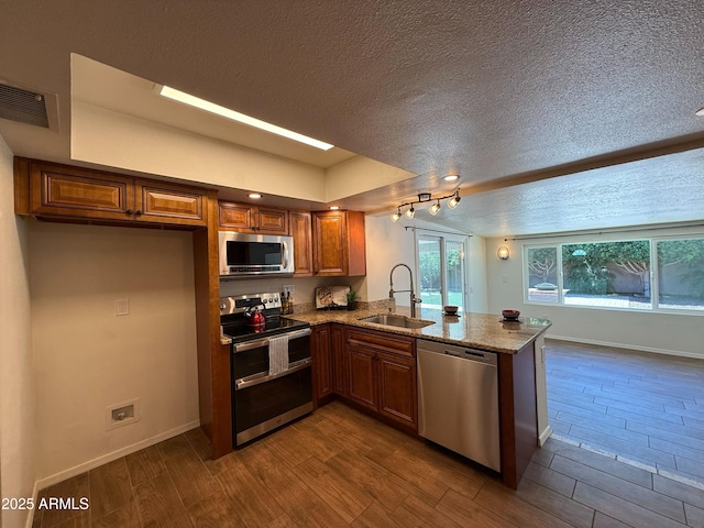 3145 W Acoma Dr, Phoenix, AZ 85053 - kitchen with appliances with stainless steel finishes, brown cabinetry, a peninsula, light stone countertops, and a textured ceiling