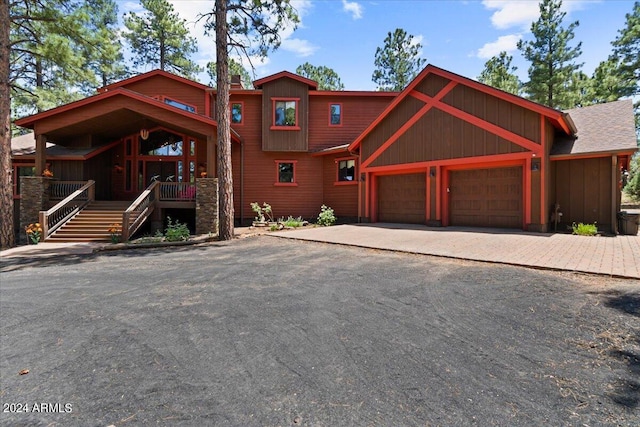 rustic home with an attached garage, asphalt driveway, and covered porch