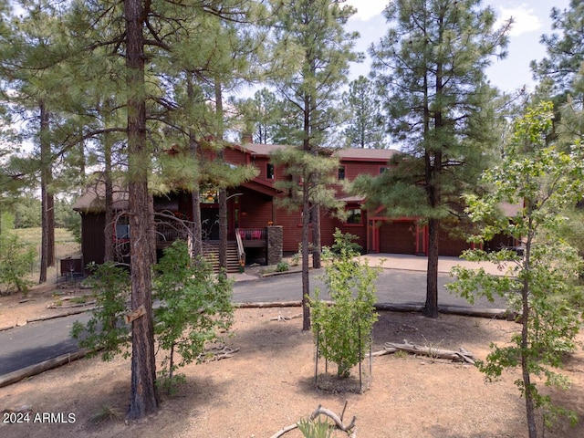 view of property hidden behind natural elements featuring driveway, a garage, a porch, and stairs