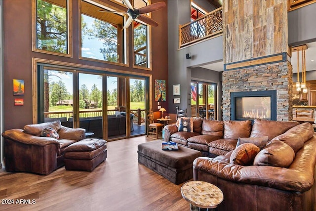 living room featuring a towering ceiling, ceiling fan, wood finished floors, and a stone fireplace