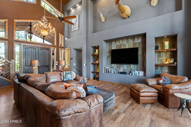 living area with a high ceiling, built in features, wood finished floors, and a chandelier