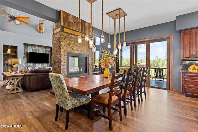 dining space with wood finished floors, a ceiling fan, a fireplace, high vaulted ceiling, and baseboards