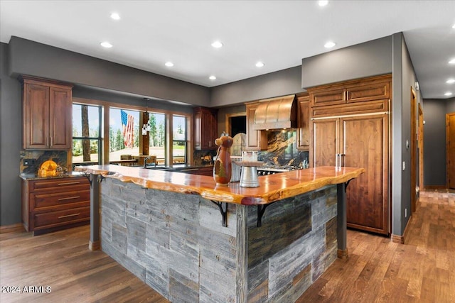 kitchen featuring custom exhaust hood, tasteful backsplash, wood finished floors, recessed lighting, and a spacious island