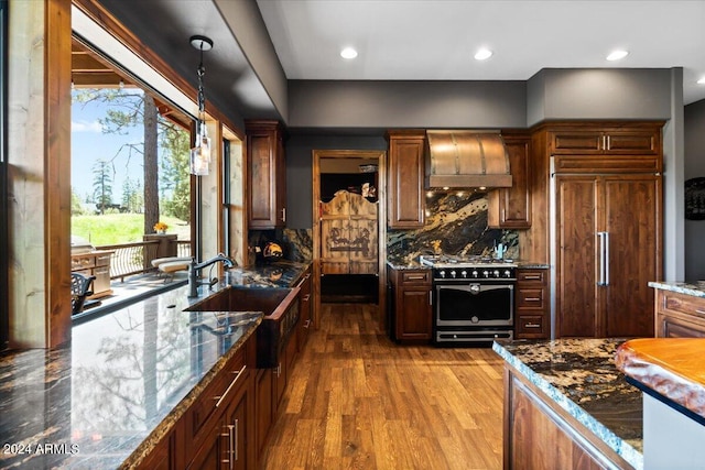 kitchen with custom exhaust hood, stainless steel gas range, paneled refrigerator, tasteful backsplash, and wood finished floors