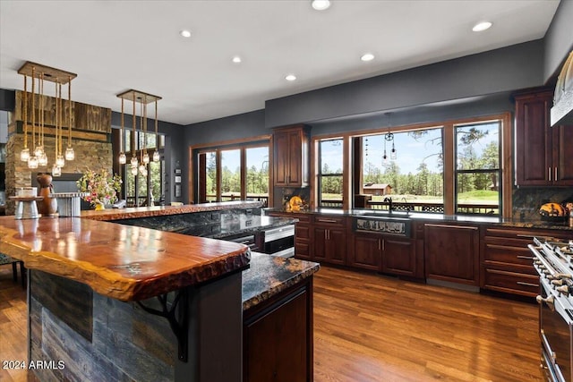 kitchen featuring dark wood-style flooring, recessed lighting, high end stove, decorative light fixtures, and a large island with sink