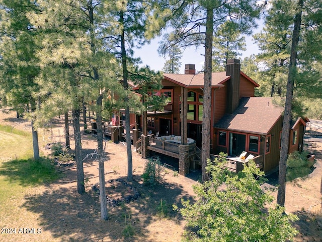 rear view of property featuring a chimney, a wooden deck, roof with shingles, and an outdoor living space