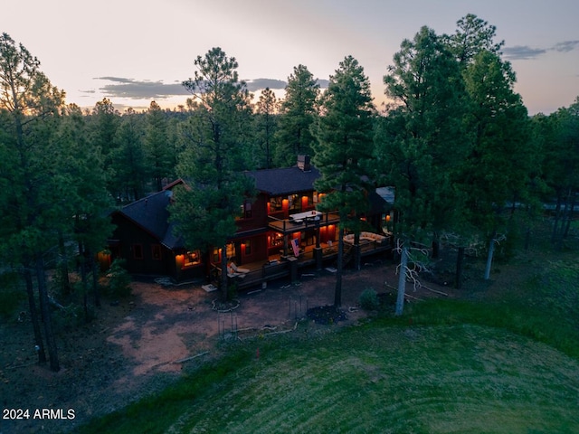 back of property at dusk featuring a forest view, a yard, and a chimney