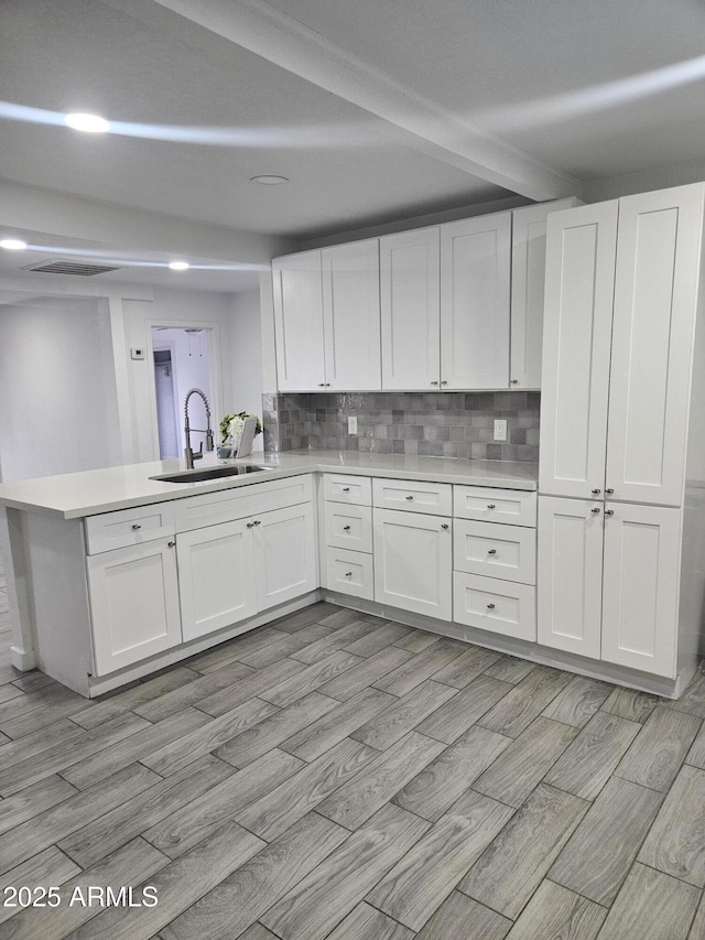 kitchen featuring backsplash, kitchen peninsula, white cabinetry, and sink