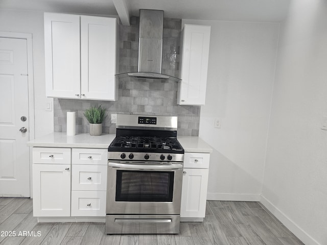 kitchen featuring stainless steel range with gas cooktop, wall chimney range hood, light hardwood / wood-style flooring, decorative backsplash, and white cabinetry