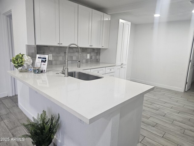 kitchen with kitchen peninsula, white cabinetry, sink, and decorative backsplash