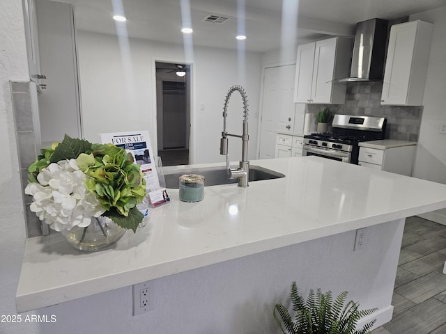 kitchen with sink, wall chimney exhaust hood, decorative backsplash, gas stove, and white cabinetry