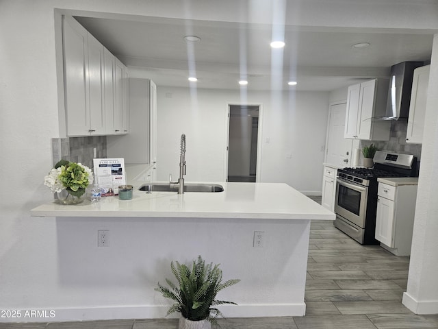 kitchen with kitchen peninsula, stainless steel gas range oven, wall chimney range hood, sink, and white cabinetry