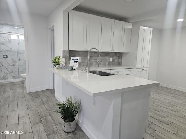 kitchen featuring kitchen peninsula, backsplash, white cabinetry, and sink