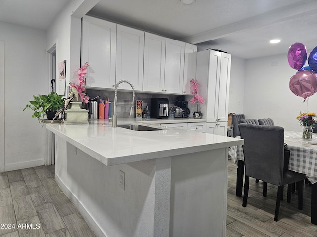 kitchen with kitchen peninsula, light stone countertops, tasteful backsplash, sink, and white cabinetry