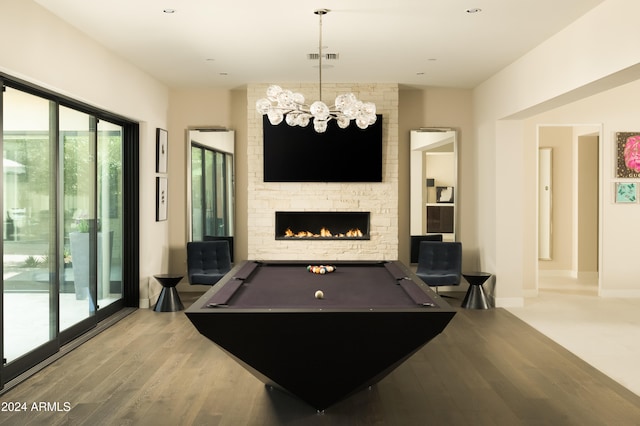 playroom with a notable chandelier, light hardwood / wood-style floors, a stone fireplace, and pool table