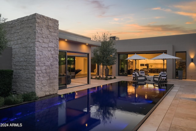 pool at dusk featuring an outdoor living space and a patio