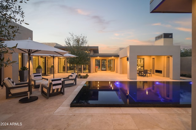 pool at dusk featuring an outdoor living space with a fireplace and a patio