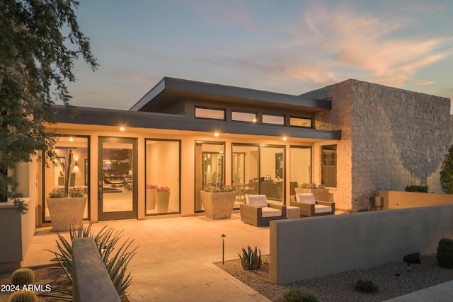 back house at dusk with outdoor lounge area and a patio