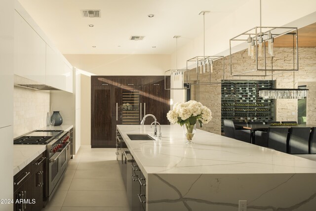 kitchen featuring white cabinets, range with two ovens, sink, a large island, and decorative light fixtures