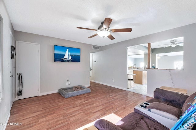 living room featuring ceiling fan, light hardwood / wood-style flooring, a textured ceiling, and sink