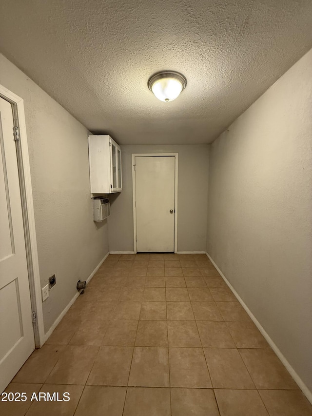 washroom featuring baseboards, an AC wall unit, light tile patterned floors, a textured ceiling, and cabinet space