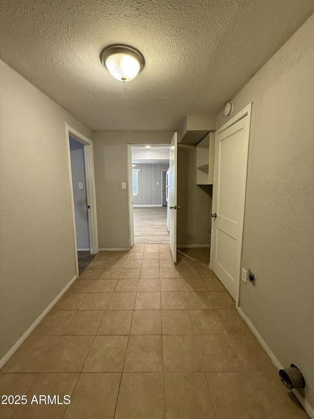 hall featuring light tile patterned floors, a textured ceiling, and baseboards