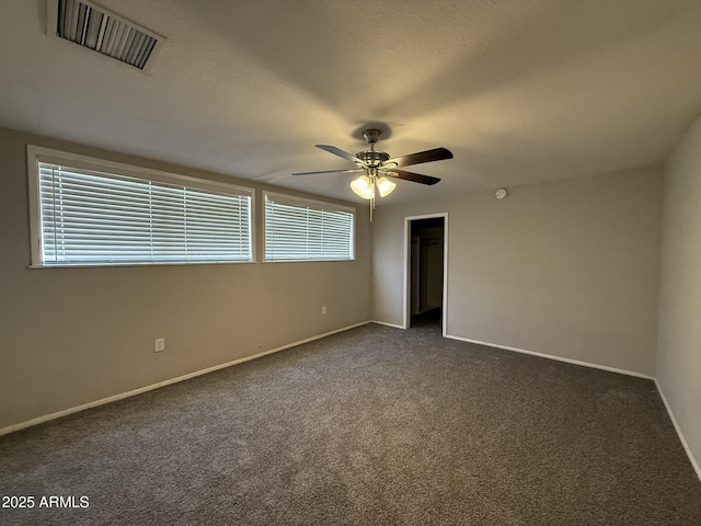 unfurnished room with dark colored carpet, visible vents, baseboards, and a ceiling fan