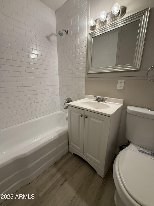 bathroom with toilet, wood finished floors, vanity, and shower / washtub combination
