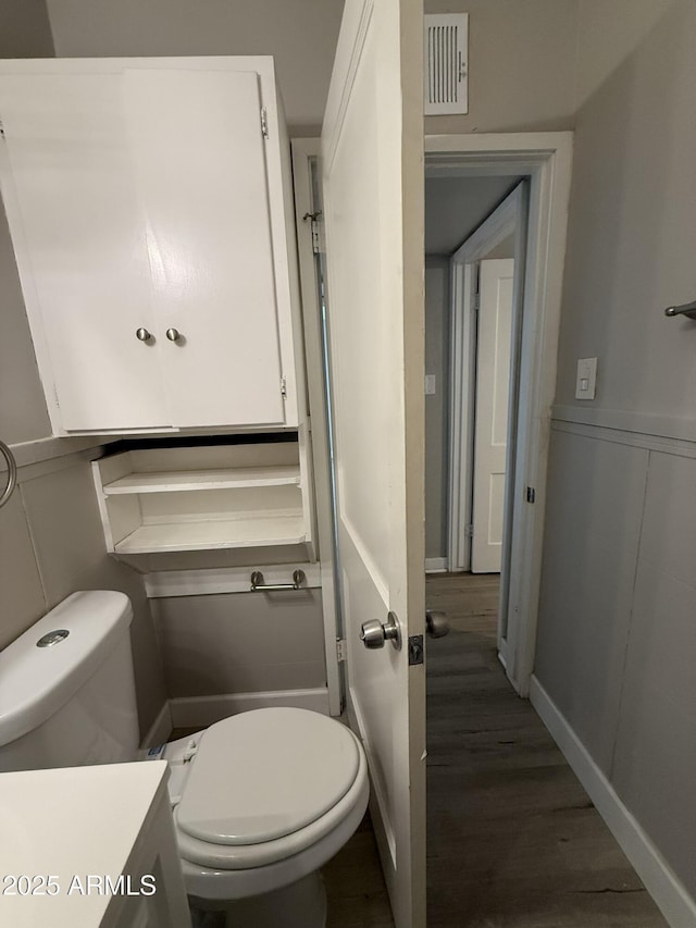 half bathroom with visible vents, toilet, and wood finished floors