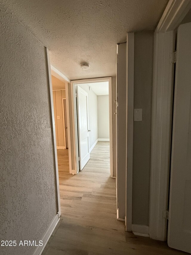 hallway with light wood-style floors, baseboards, and a textured ceiling