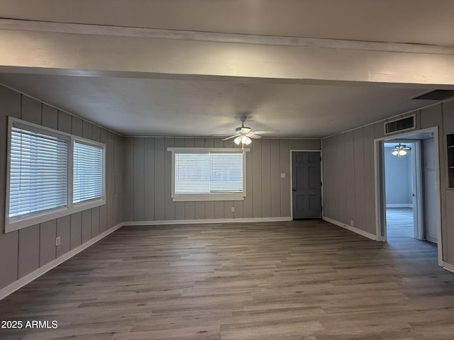 unfurnished living room with plenty of natural light, visible vents, a ceiling fan, and wood finished floors