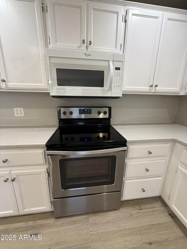 kitchen featuring white microwave, stainless steel range with electric cooktop, light countertops, and white cabinets