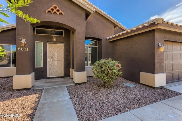 property entrance with a tile roof, an attached garage, and stucco siding