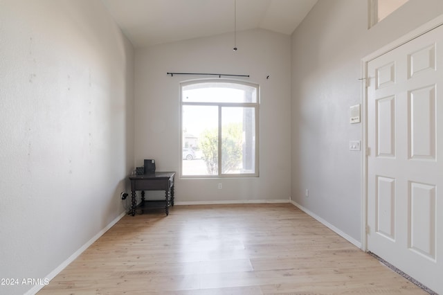 empty room featuring light wood-type flooring, baseboards, and vaulted ceiling