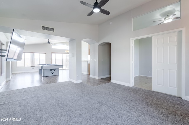 unfurnished living room with arched walkways, carpet floors, vaulted ceiling, and visible vents