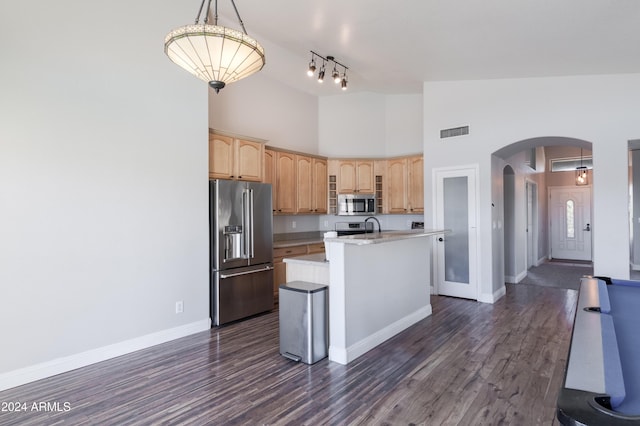 kitchen with arched walkways, a kitchen island with sink, stainless steel appliances, baseboards, and pendant lighting