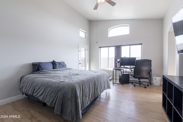 bedroom featuring light wood-style floors, a high ceiling, ceiling fan, and baseboards