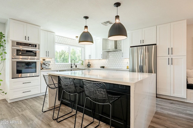 kitchen with light wood-style flooring, stainless steel appliances, a kitchen island, wall chimney exhaust hood, and tasteful backsplash