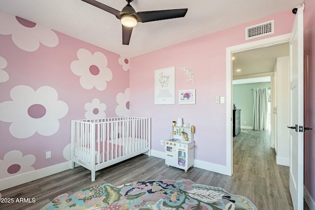 bedroom featuring a nursery area, visible vents, and wood finished floors