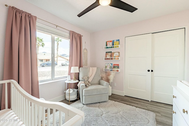 bedroom with a crib, a closet, wood finished floors, and baseboards