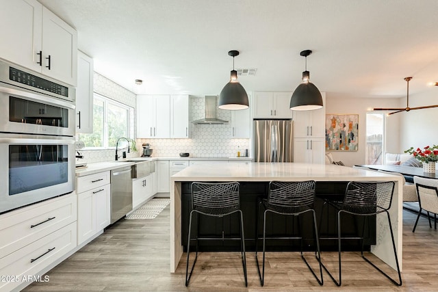 kitchen with stainless steel appliances, a kitchen island, a sink, visible vents, and wall chimney exhaust hood