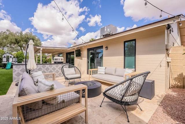 view of patio with central AC unit, a playground, and an outdoor living space with a fire pit