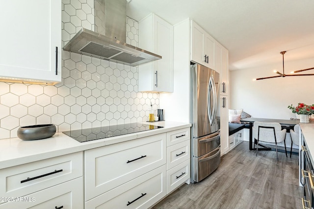 kitchen featuring black electric stovetop, backsplash, freestanding refrigerator, white cabinets, and wall chimney exhaust hood