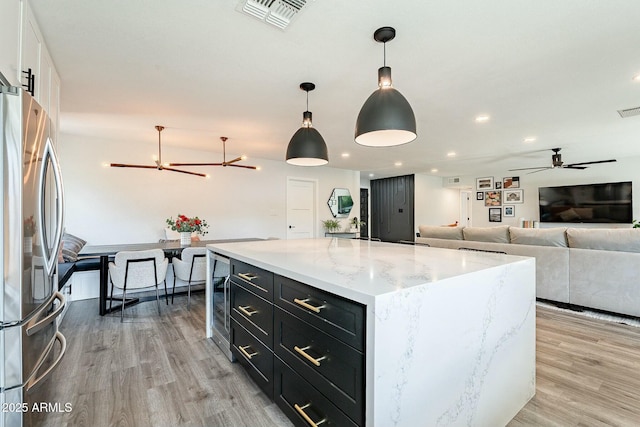 kitchen with light wood-style flooring, a kitchen island, visible vents, dark cabinetry, and freestanding refrigerator