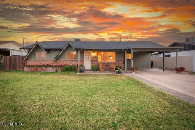 view of front of property with an attached carport, brick siding, fence, driveway, and a lawn