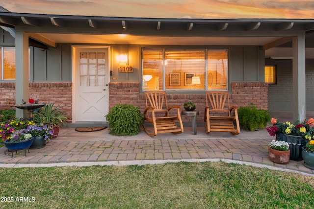 property entrance featuring board and batten siding, brick siding, and a porch