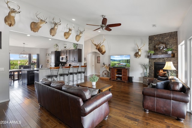 living room featuring lofted ceiling, dark wood-type flooring, a stone fireplace, and ceiling fan