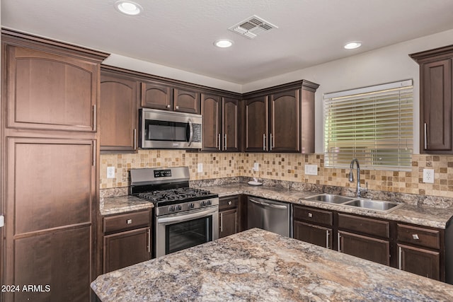 kitchen featuring tasteful backsplash, light stone counters, appliances with stainless steel finishes, dark brown cabinetry, and sink